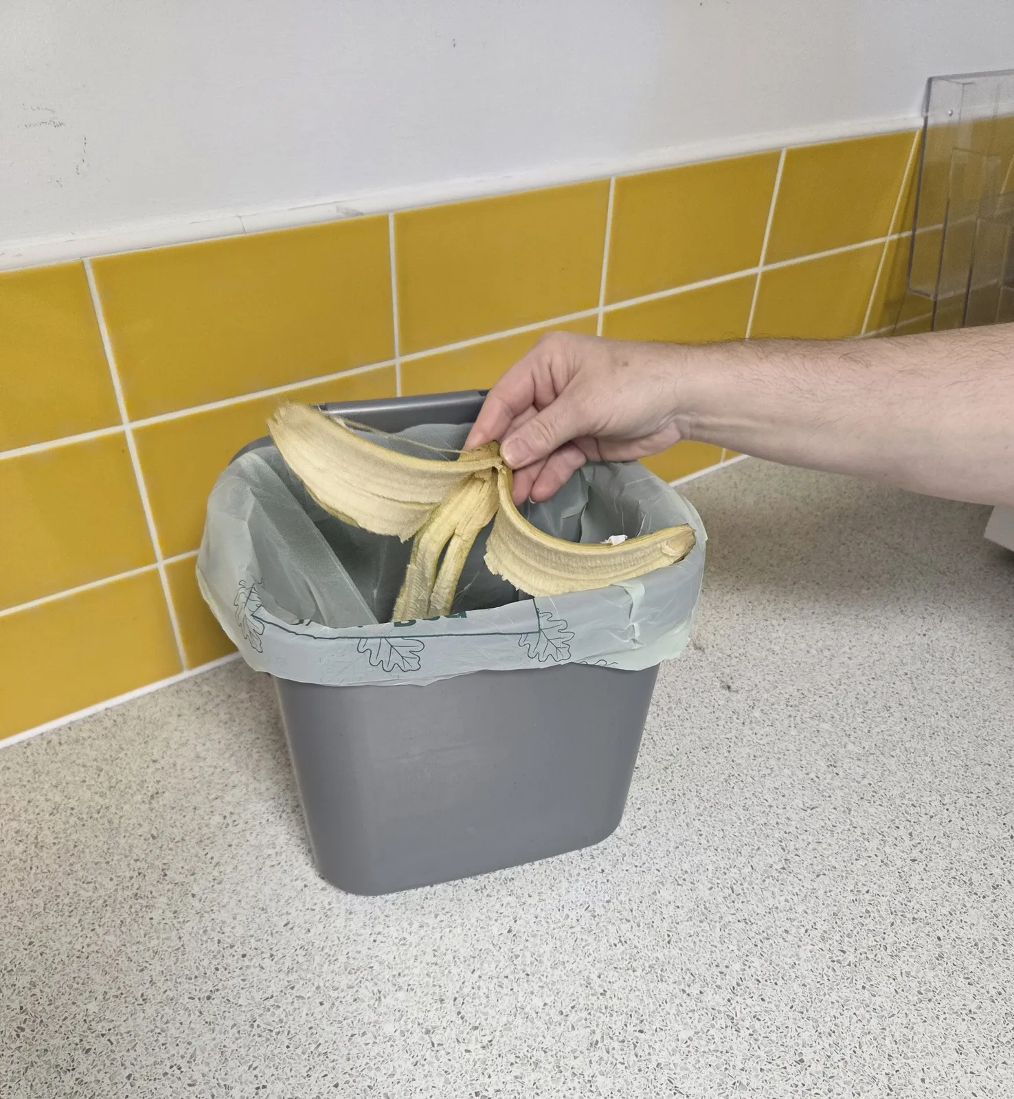Someone putting a banana peel into a grey food waste caddie sitting atop the kitchen counter