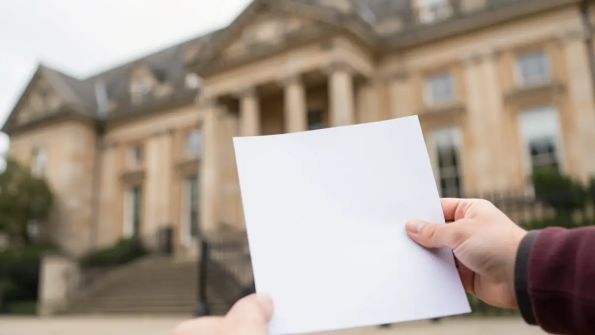 Generic image of a hand holding a grant application form with a blurred council building in the background.